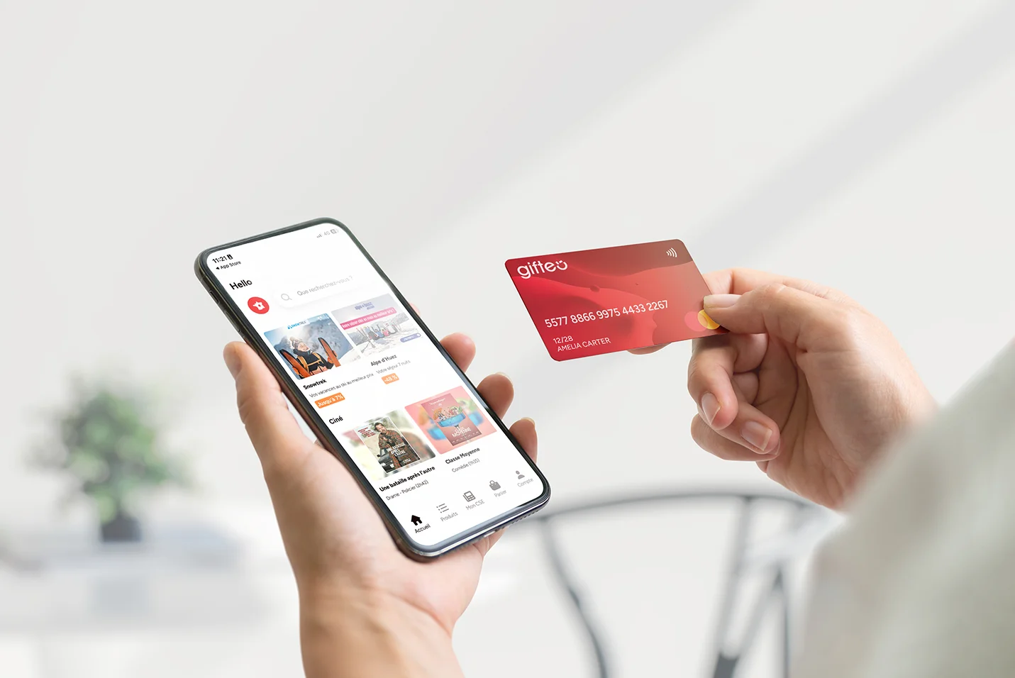 Person holds a smartphone showing a mobile wallet app while a red card is tapped against it to pay.